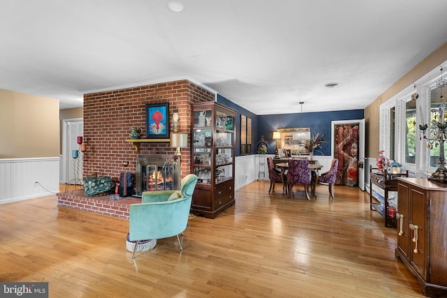 living area with light wood-type flooring, a brick fireplace, and a wainscoted wall