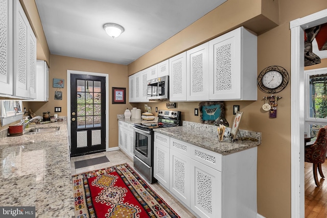 kitchen featuring a sink, stainless steel appliances, white cabinets, baseboards, and light stone countertops