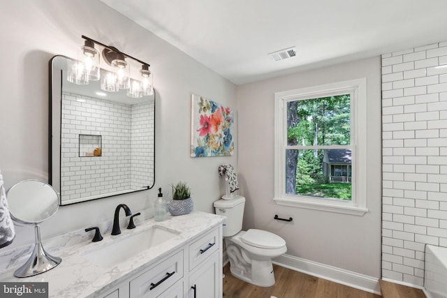bathroom with wood finished floors, toilet, vanity, baseboards, and a shower