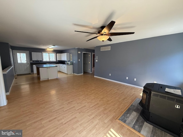 unfurnished living room with a wood stove, visible vents, light wood-style floors, baseboards, and ceiling fan