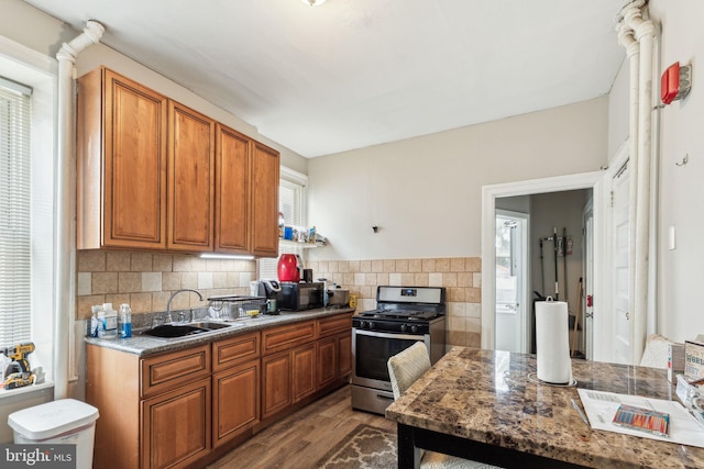 kitchen with stainless steel range with gas stovetop, a sink, dark wood finished floors, backsplash, and brown cabinetry