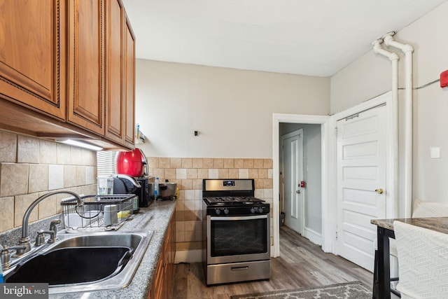 kitchen with tasteful backsplash, wood finished floors, a sink, brown cabinets, and stainless steel gas range