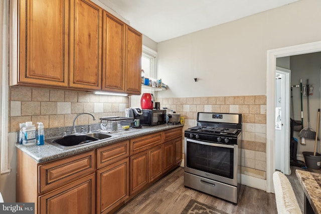 kitchen with a sink, tasteful backsplash, wood finished floors, brown cabinets, and stainless steel gas range oven