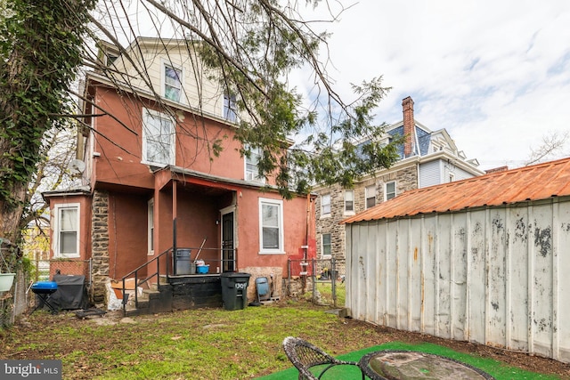 back of house with a lawn, an outbuilding, a storage unit, and stucco siding
