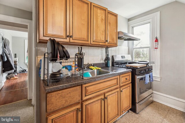 kitchen with dark countertops, decorative backsplash, gas stove, brown cabinetry, and under cabinet range hood