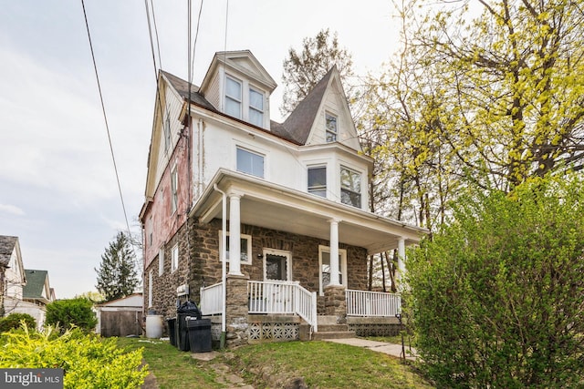 victorian house with stucco siding, stone siding, and covered porch