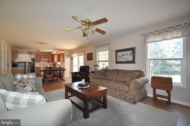 living room with ceiling fan, baseboards, and light wood-type flooring