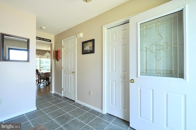 foyer entrance featuring baseboards and dark tile patterned flooring