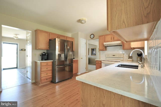 kitchen with white electric range oven, a sink, light countertops, stainless steel refrigerator with ice dispenser, and under cabinet range hood