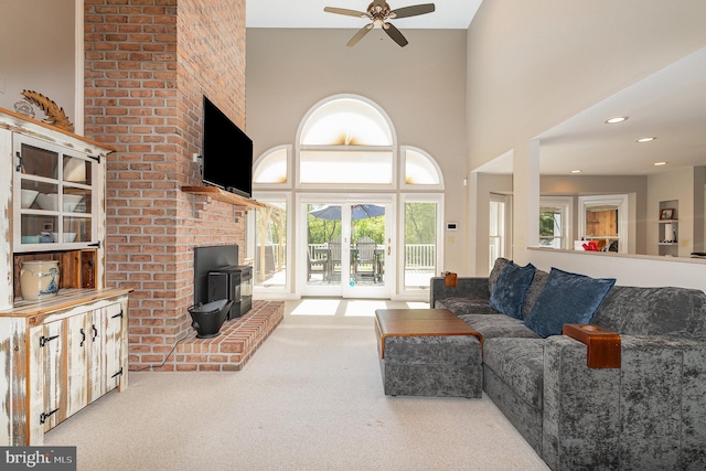 living room featuring a wood stove, a towering ceiling, ceiling fan, plenty of natural light, and carpet