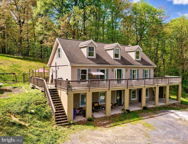 view of front of house with a deck, stairway, a patio area, and roof with shingles