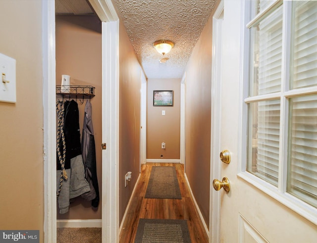 hall with a textured ceiling, wood finished floors, and baseboards