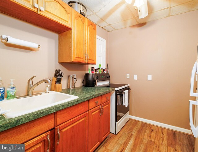 kitchen featuring white electric stove, a sink, light wood-type flooring, baseboards, and dark countertops