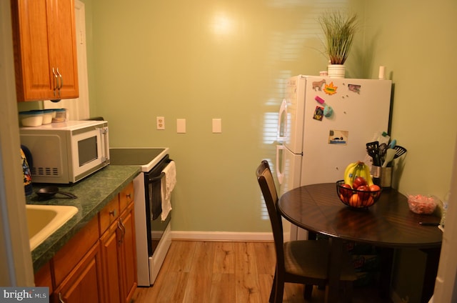 kitchen featuring white appliances, light wood-style flooring, baseboards, dark countertops, and brown cabinets