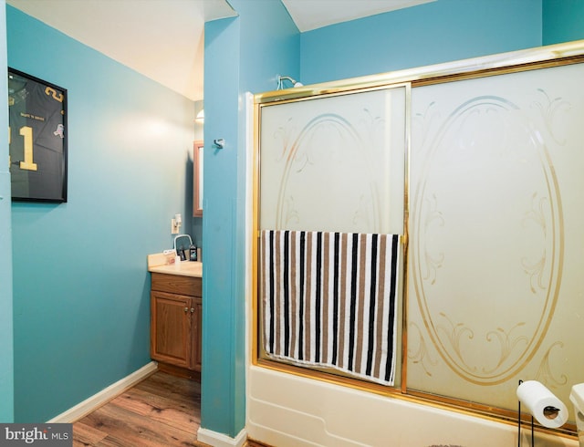 bathroom featuring wood finished floors, baseboards, combined bath / shower with glass door, and vanity