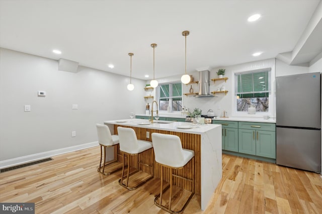 kitchen featuring wall chimney range hood, green cabinets, light countertops, visible vents, and freestanding refrigerator