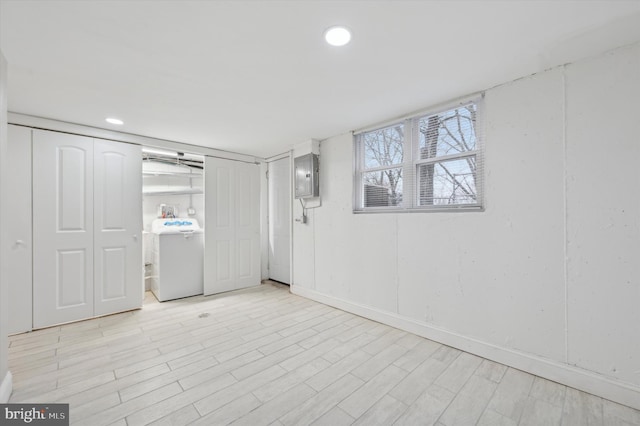 below grade area with electric panel, light wood finished floors, baseboards, washer / clothes dryer, and recessed lighting