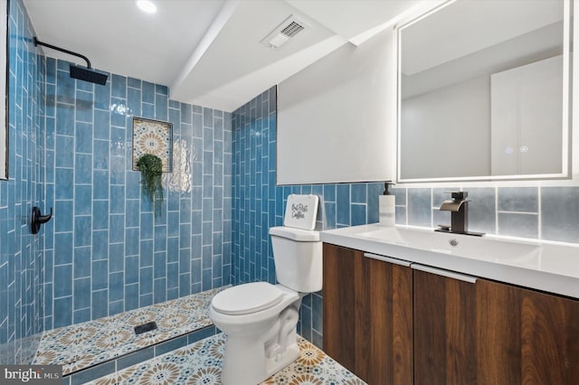 full bath with a tile shower, visible vents, toilet, vanity, and tile walls