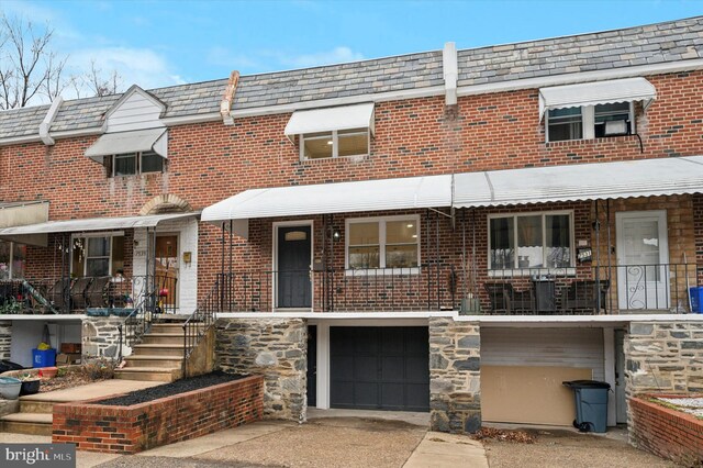 view of property with an attached garage, driveway, brick siding, and mansard roof