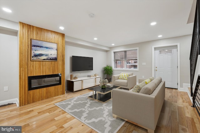 living area featuring a glass covered fireplace, wood finished floors, recessed lighting, and stairs