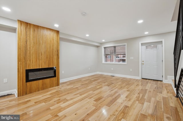 unfurnished living room with baseboards, recessed lighting, wood finished floors, a large fireplace, and stairs