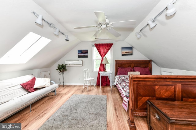 bedroom featuring track lighting, an AC wall unit, vaulted ceiling with skylight, and light wood-style flooring