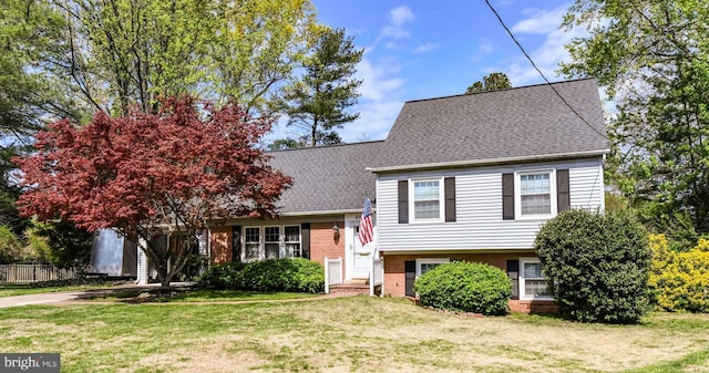 split level home featuring a front lawn, brick siding, and a shingled roof