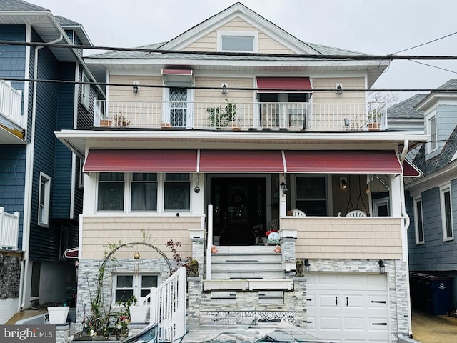 view of property featuring stone siding, a balcony, and a garage