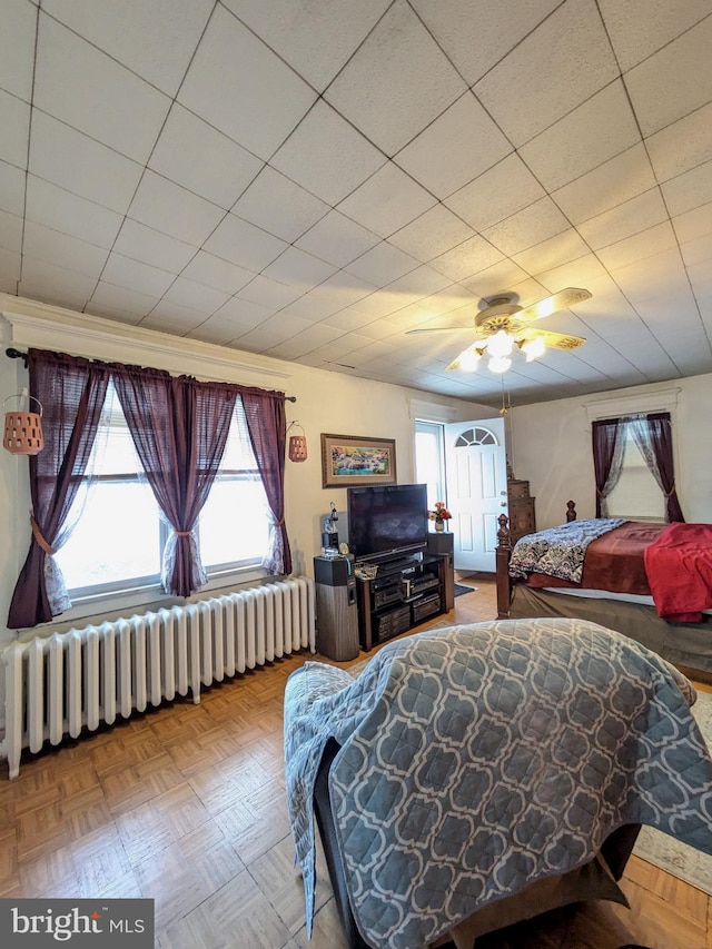 bedroom with multiple windows, ceiling fan, and radiator