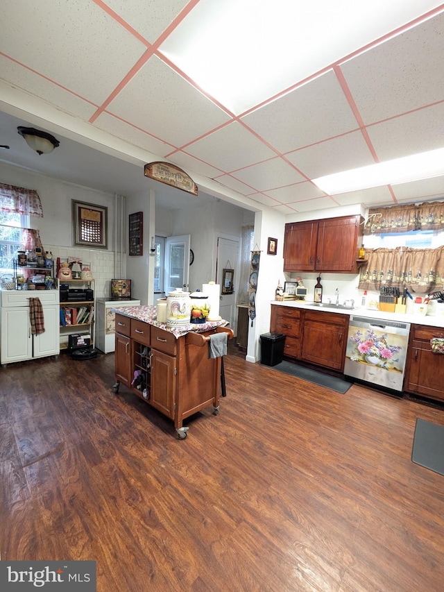 kitchen with light countertops, stainless steel dishwasher, a sink, dark wood-type flooring, and a kitchen island