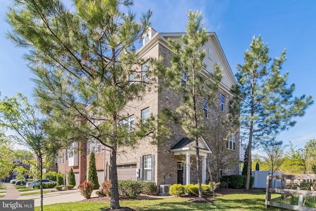 view of front of home featuring driveway, a front yard, a garage, brick siding, and central AC
