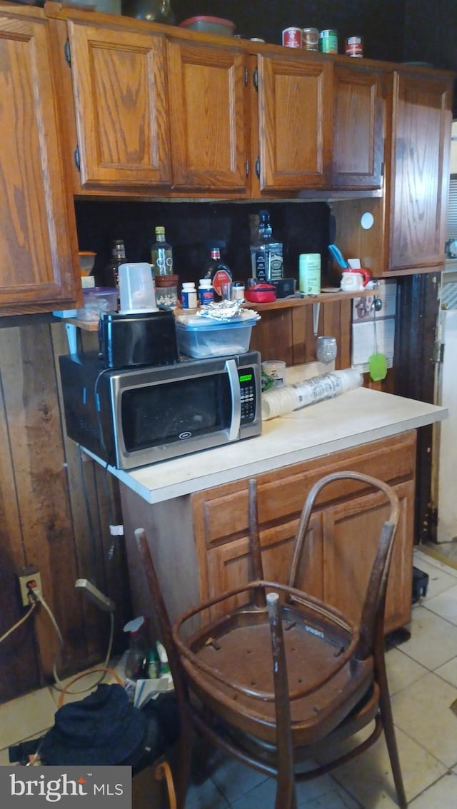 kitchen featuring brown cabinetry, light tile patterned floors, light countertops, and stainless steel microwave