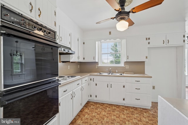 kitchen with a sink, dobule oven black, ceiling fan, light countertops, and under cabinet range hood