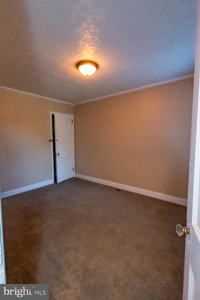 empty room with crown molding, carpet flooring, and baseboards