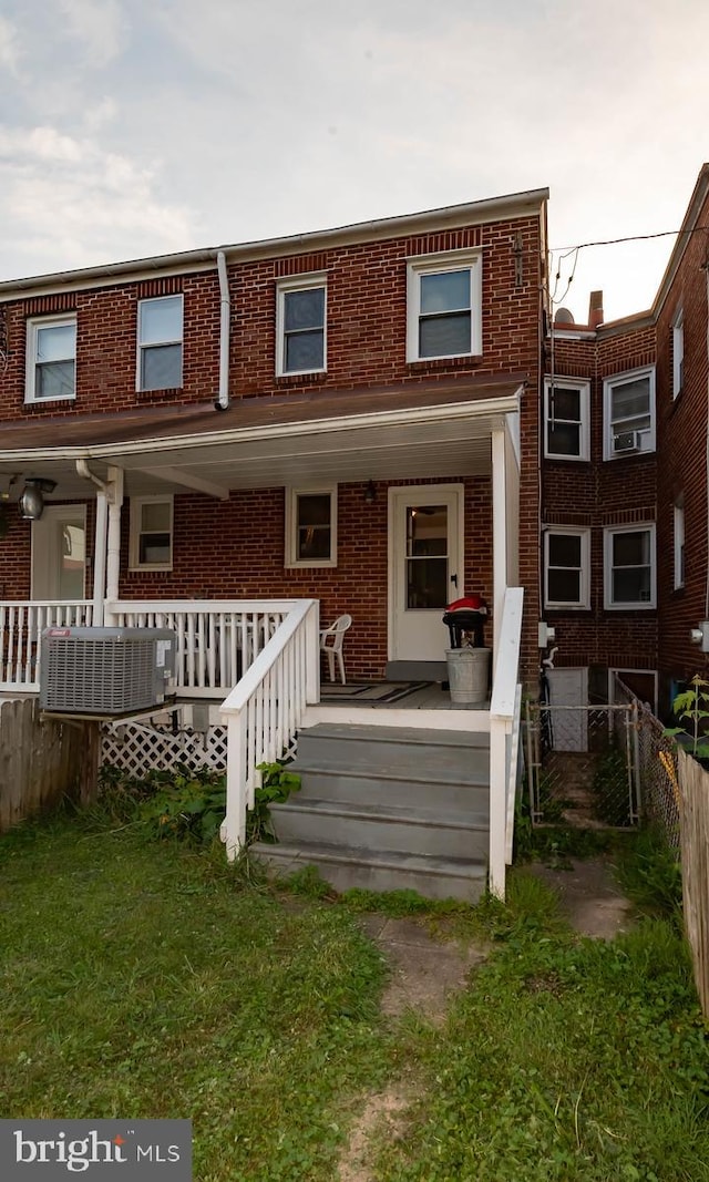 rear view of house with brick siding, a porch, and fence