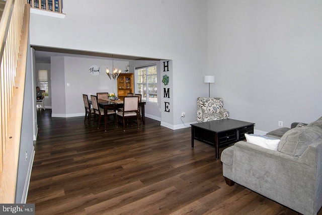 living area featuring baseboards, a notable chandelier, dark wood finished floors, and a high ceiling