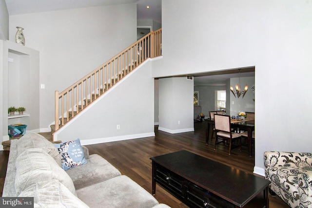 living area with a towering ceiling, wood finished floors, baseboards, stairway, and a notable chandelier