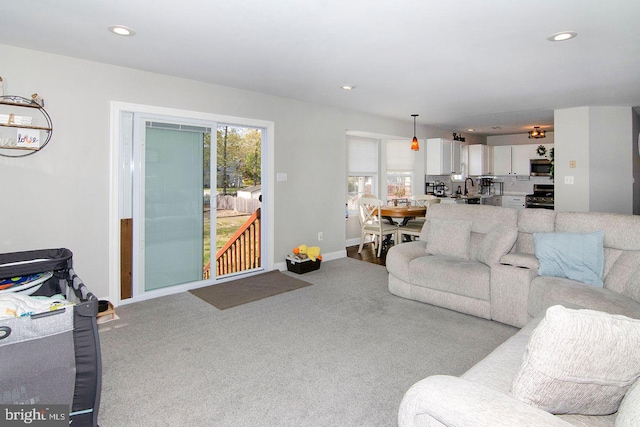 carpeted living area featuring recessed lighting, a sink, and baseboards