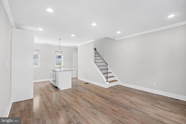 unfurnished living room with light wood finished floors, a sink, crown molding, visible vents, and stairway