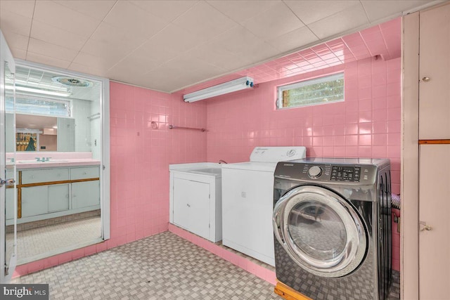 clothes washing area with laundry area, light floors, a sink, independent washer and dryer, and tile walls