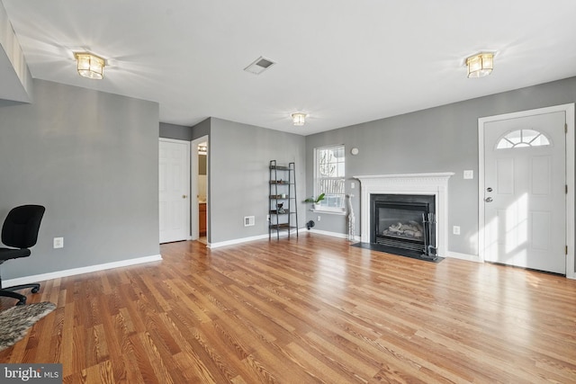 unfurnished living room with baseboards, visible vents, light wood-type flooring, and a fireplace with flush hearth