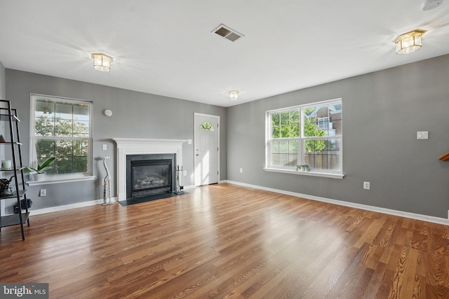 unfurnished living room with a fireplace with flush hearth, wood finished floors, visible vents, and baseboards
