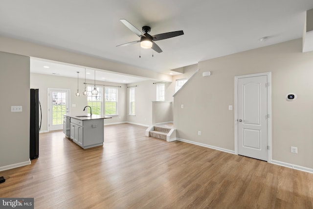 unfurnished living room featuring light wood-style flooring, baseboards, ceiling fan, and a sink