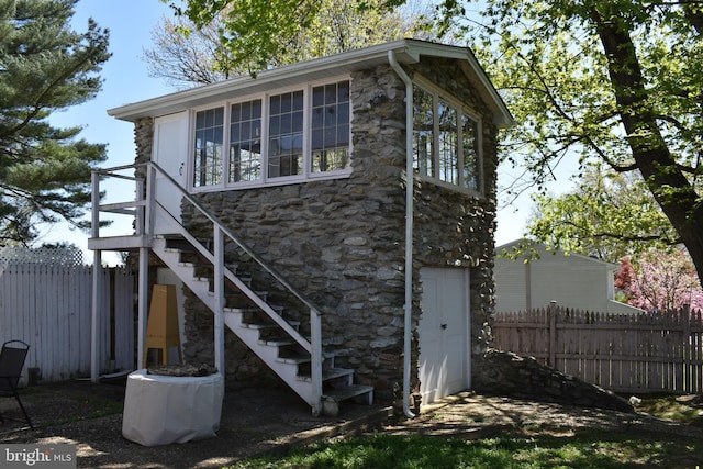 rear view of property featuring fence, stone siding, and stairs