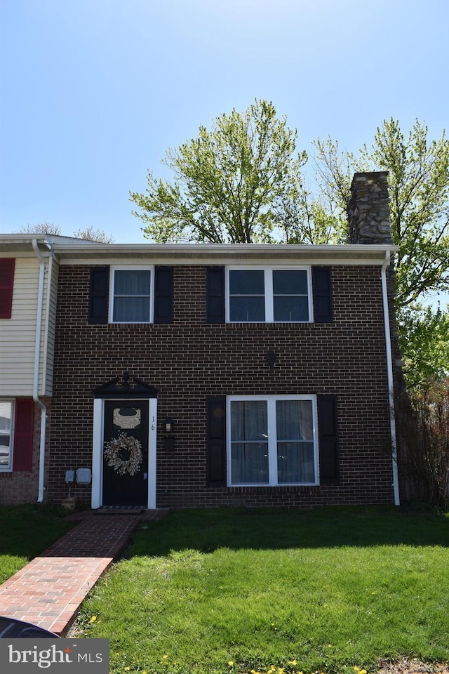 view of front of house featuring a chimney, a front lawn, and brick siding