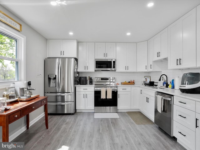 kitchen with stainless steel appliances, light countertops, a sink, tasteful backsplash, and white cabinetry