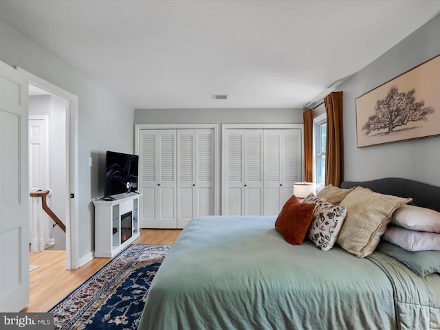 bedroom featuring visible vents, a glass covered fireplace, light wood-style floors, and two closets