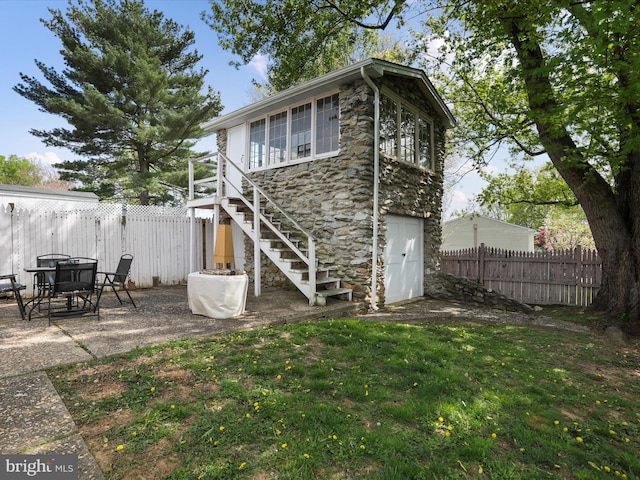 back of house with a fenced backyard, stone siding, stairs, a yard, and a patio