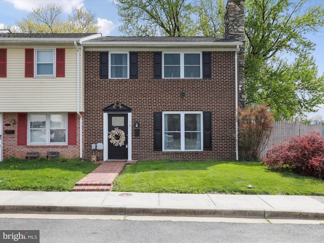 townhome / multi-family property featuring a chimney, brick siding, fence, and a front yard