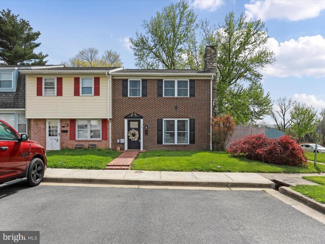 view of property featuring brick siding, a front yard, and a chimney